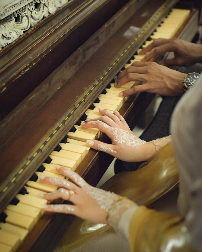 about-02 Elegant hands play a duet on a vintage piano, showcasing intricate henna design.