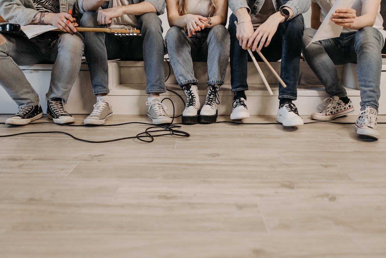 Group of musicians sitting in a casual setting ready for band rehearsal, wearing denim and sneakers.